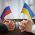 Ukraine and Russia Flag at ta table with two sets of hands.
