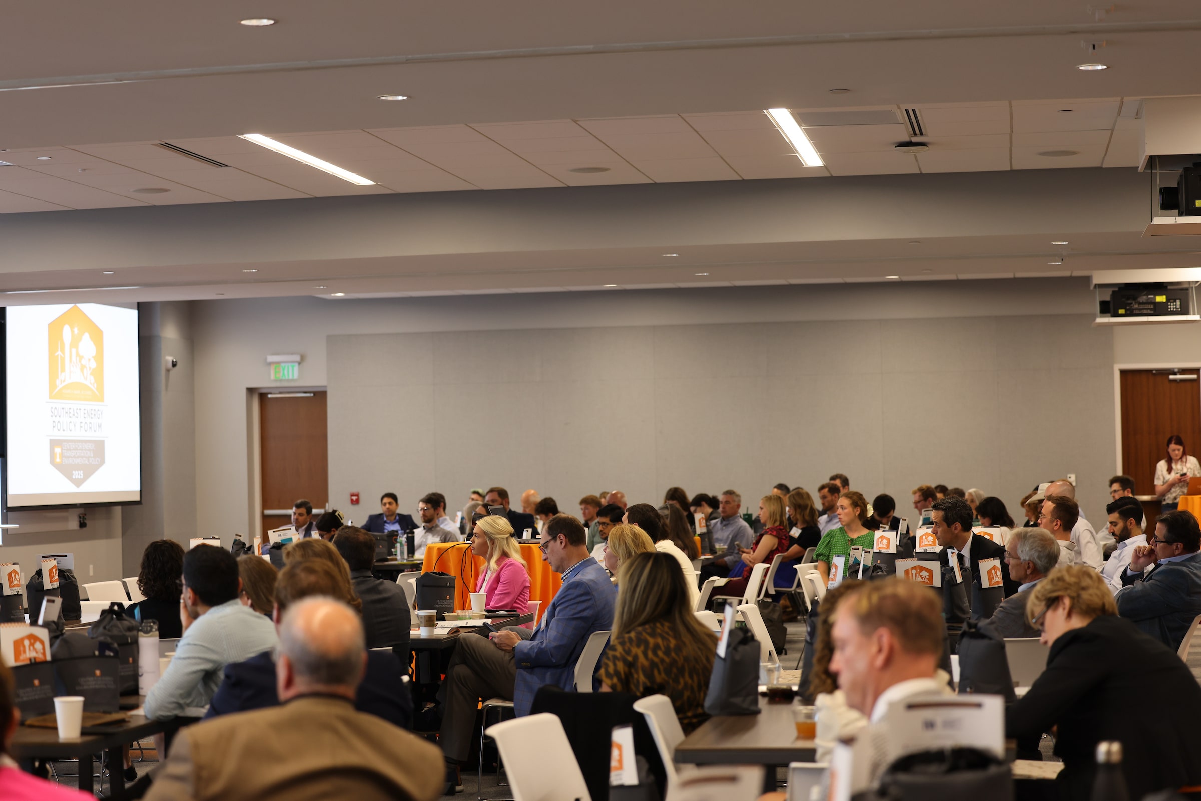 Conference room full of people watching speaker from a side view.